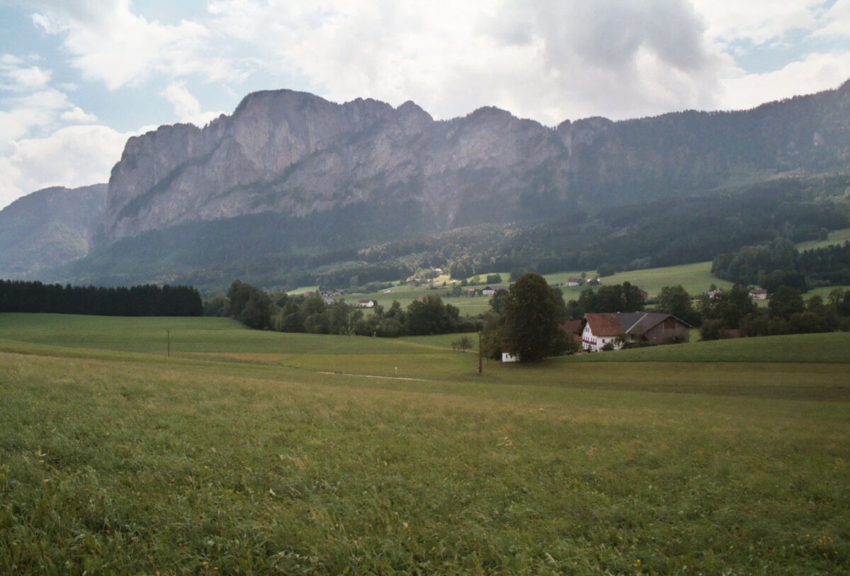 Grüne Wiese mit einem Haus, fotografiert Richtung Bergmassiv